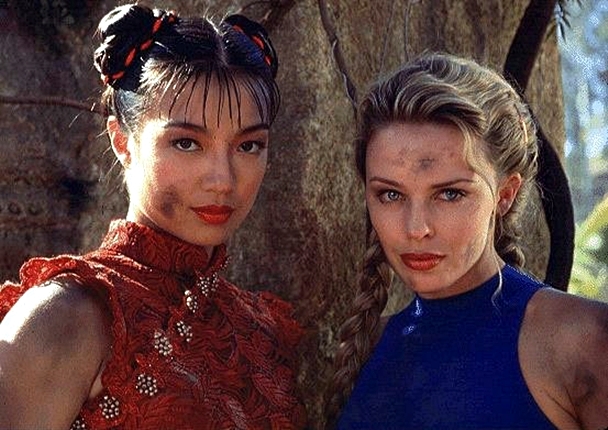 Actresses Ming-Na Wen, in a red garment, and Kylie Minogue, in a blue garment, as Chun-li and Cammy in the movie Street Fighter. They are staring into the camera and their faces are dirty.