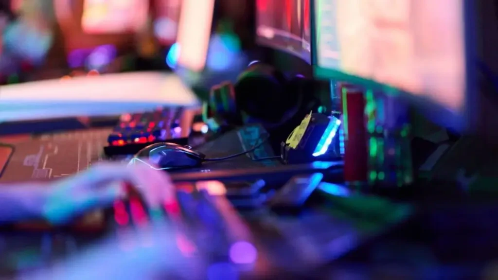 Mãos digitando em teclado gamer iluminado em frente a monitores, ilustrando o impacto do vício em apostas online na saúde mental.