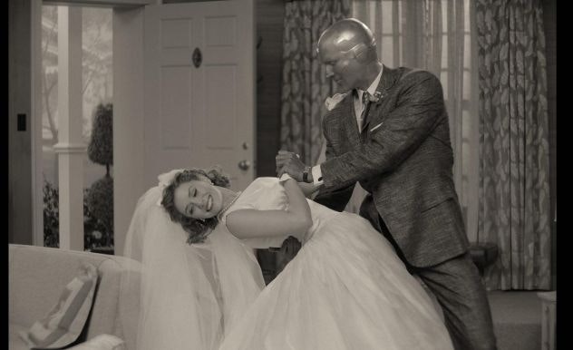 A woman in a white wedding dress is dipped down in a dance move by her robot husband in a tuxedo