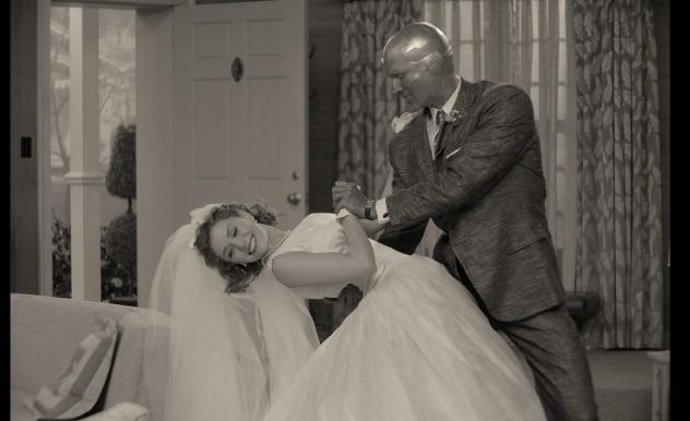 A woman in a white wedding dress is dipped down in a dance move by her robot husband in a tuxedo