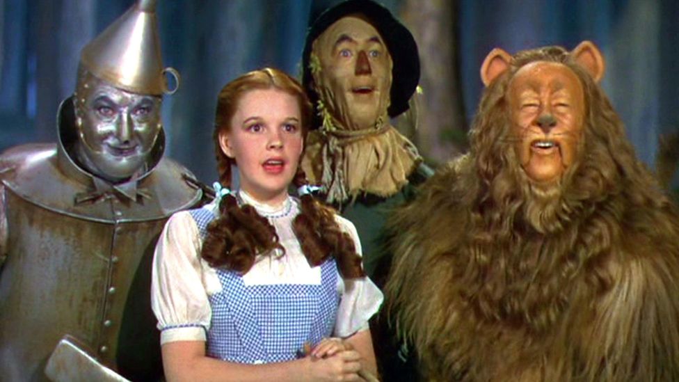The main characters from The Wizard of Oz look off smiling at something in the distance
